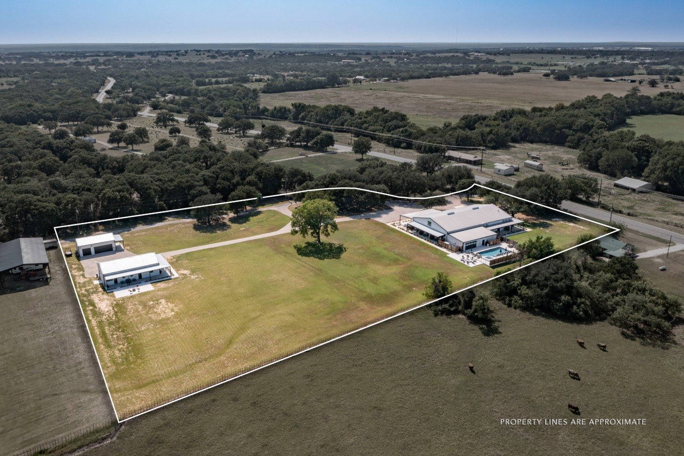 Aerial with the parcel boundary outlined — main barndominium and pool at right, mini barndominium and shop at left