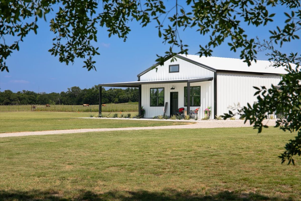 Mini barndominium exterior — covered porch, standing seam roof, pasture beyond