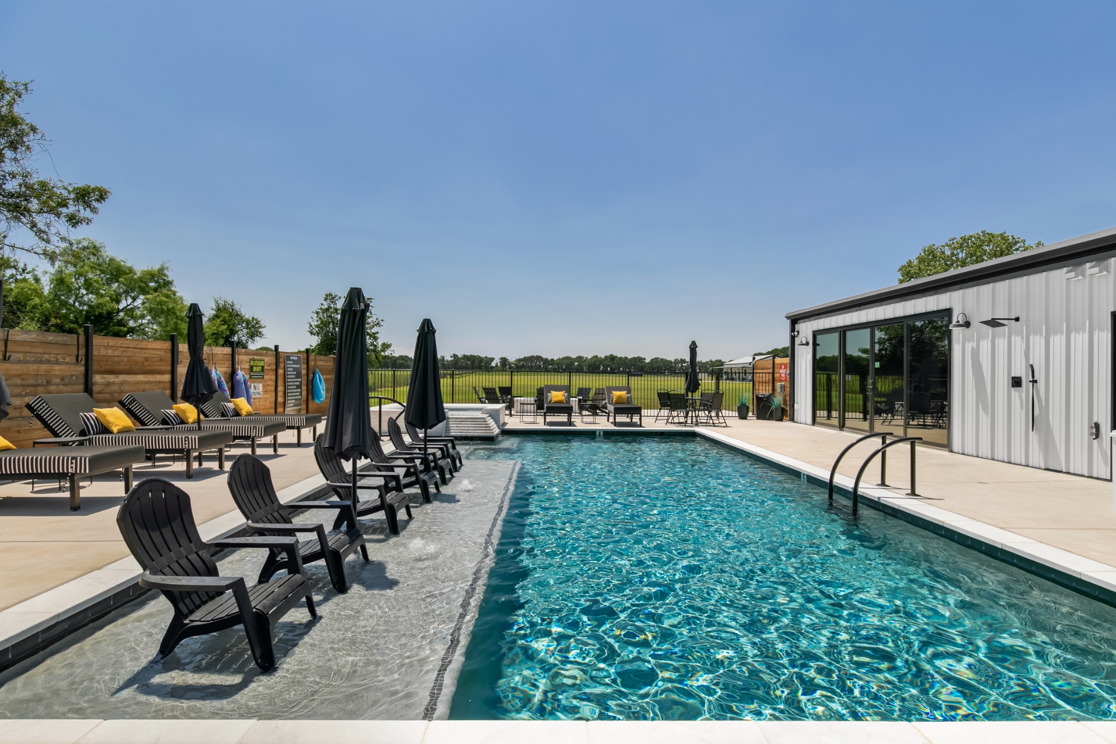 Pool and spa complex — tanning ledge with chairs in the water, lounge seating, pool house with outdoor showers